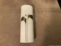 Front view of the tall white ceramic bud vase with golden calla lily decoration on the surface.