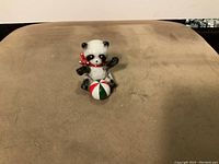 Front view of the vintage ceramic panda figurine sitting with a color-segmented ball and red bow on a beige surface.