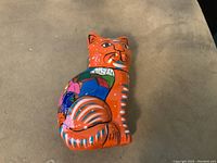 Front and right side of a brightly colored ceramic cat figurine, orange base with blue, purple, and pink floral and abstract decorations.