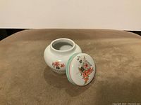 White ceramic jar with matching lid placed beside it, floral patterns visible on body and lid, jar opening visible