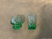Two uranium green depression glass shot/liquor glasses, one short and round, one taller and cylindrical, both etched and positioned on tan fabric.