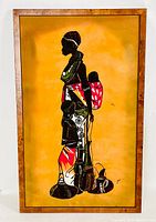 Full view of framed painting on fabric depicting an African woman carrying a child, set against an orange warm background with colorful traditional patterns on figures.