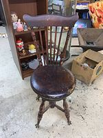 Front view of antique wooden swivel chair with curved backrest and round seat in worn condition showing scuffs and scratches.