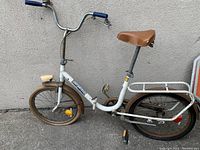 Full side view of the white Barbarella vintage bicycle with brown saddle and blue handle grips, showing the rear carrier rack and tires.