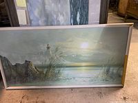 Front view of oil painting showing beach, lighthouse, sunset, and rocky coastline in a wooden frame with frame wear.