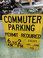 Photo showing the full front view of the rectangular yellow metal sign with black text detailing commuter parking permit rules. Shows wear and scratches.