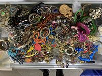 Top-down view showing the full assortment of mixed costume jewelry including bracelets, necklaces, earrings, and brooches in various colors and materials.