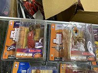 Close-up photo of LeBron James figure dunking in Cavaliers uniform and Yao Ming shooting in Rockets uniform, clearly visible NBA and McFarlane branding on packaging