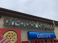 Metal neon sign reading "off-track betting" mounted on building facade