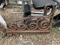 Side view of heavy cast iron bracket showing scroll design and rough, rusty patina.