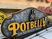 Front view of Potbelly Sandwich Shop sign showing raised yellow and white lettering with stove graphic and patterned background.