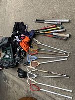 Lot photographed on concrete floor showing lacrosse sticks, baseball bats, helmet, apparel, and bag spread out
