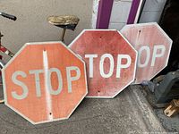 Three octagonal stop signs leaning against a wall, showing wear and faded red paint with white STOP lettering.