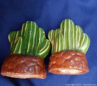 Pair of green ceramic cactus bookends showing front and base details on a blue cloth background.