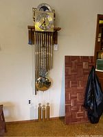 Front view of caseless wall-mounted clock movement hanging on wooden board with chime tubes and weights