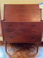 Front view of drop-front closed showing three drawers, inset oval pulls, keyhole