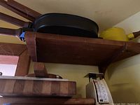 Shelf holding two black enameled Dansk square pans, yellow enameled pot and butcher block cutting board.