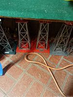 Photo showing four metal support towers in red and green colors with lattice framework on a tiled floor.