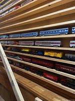 Multiple rows of plastic and metal train cars on wooden shelves, including passenger coaches, boxcars, and freight pieces