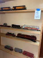 Three wooden shelves displaying a variety of train pieces including locomotives and cars.