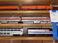 Shelf overview showing two Southern Pacific F7 locomotives on top, Western Pacific locomotive beneath, and Amtrak locomotive plus two Superliner cars on lower shelf