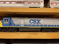 Blue and yellow CSX diesel locomotive #8704 on wooden shelf