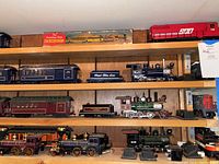 Wooden shelves displaying multiple American Flyer locomotives and cars, including red SOO Line diesel and Frontiersman box