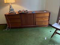 Front full view of long low wooden dresser on green carpet with lamp and metal items on top