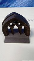 Front view of one vintage cast metal bookend featuring gothic arch design.