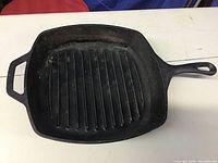Top-down view of square cast iron grill pan showing grill ridges, handles, and wear marks