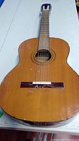 Full frontal view of Simpsons Sears acoustic guitar showing main body and neck, natural wood finish with signs of damage and wear at the bottom edge.