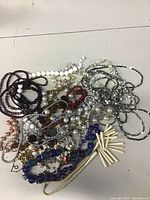 Photo of a tangled assortment of costume necklaces featuring various faux pearls, beads, and chains in multiple colors taken on a white surface.