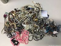 Photo showing a large tangled collection of costume jewelry consisting of various necklaces, chains, bangles, and watches.