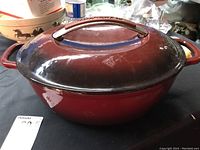 Red KitchenAid oval Dutch oven viewed from the side, showing enamel finish and side handles.