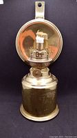 Full view of the brass oil lamp with a circular backplate, showing the wick area and the base.