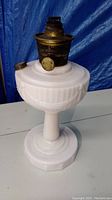 Full view of white glass pedestal oil lamp with brass burner on top, no chimney included.