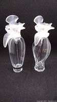 Two clear glass Nina Ricci perfume bottles with frosted glass dove caps standing side by side on black background.