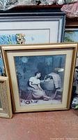Framed print showing a woman in a seated pose beside a basket with two cats nearby.
