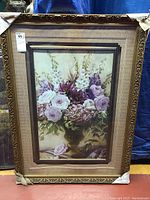 Full view of the double framed floral print showing the arrangement of purple and white flowers in a gold vase, with ornate gold frame and beige mat.
