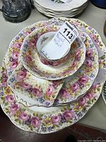 Top view of stacked plates, bowl, and sugar bowl showing floral pattern with pink, yellow, and purple flowers and gold rims