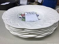 Stack of six white Wedgwood porcelain plates showing embossed lattice rim and visible floral center on top plate.