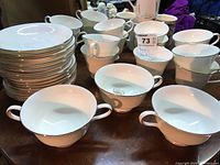 Wide shot of the full set showing a stack of plates, multiple teacups, saucers, and three two-handled soup bowls in white with silver trim.