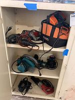 Photo of cabinet shelves containing multiple corded power tools including drills, saws, a tool bag, and battery packs.