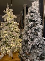 Two 7-foot flocked artificial Christmas trees side by side indoors, one lit with warm white lights, the other unlit.