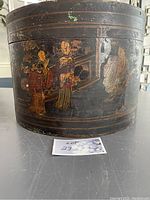 Front view of the antique wooden hat box showing hand painted Asian figures, highlighting the wear and paint loss.