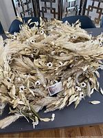 Top view of six cream-colored garlands showing dried pampas grass, beige leaves, and white flowers grouped together on a black surface.