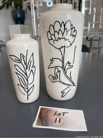 Front view of two white ceramic vases with black hand-painted botanical designs and Lot 11 sign.
