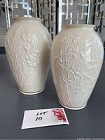 Two white Lenox ceramic vases with raised floral patterns placed next to each other on a table.