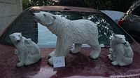 Photo showing set of three white polar bear decorative figurines placed on a car hood, includes one large standing bear and two smaller bears (one with cub).