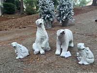 Photo showing all four white polar bear figurines arranged on ground with two small pine trees in background